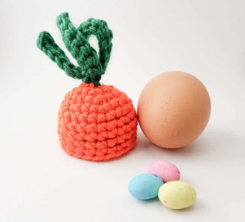 Crochet carrot top egg cosy next to a chicken egg