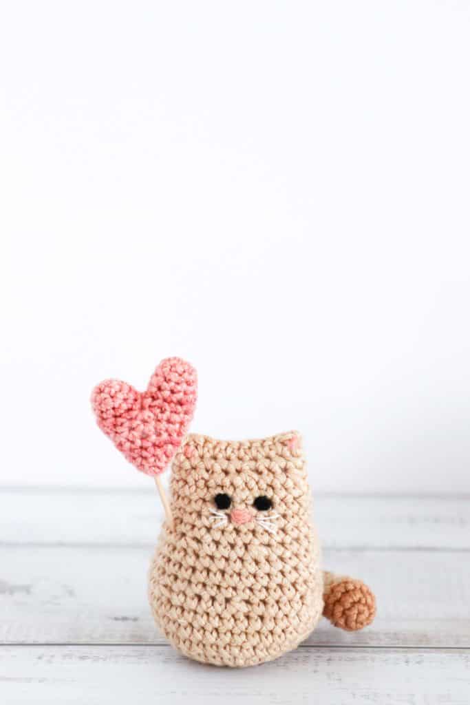 a crochet valentine cat with a pink crochet heart