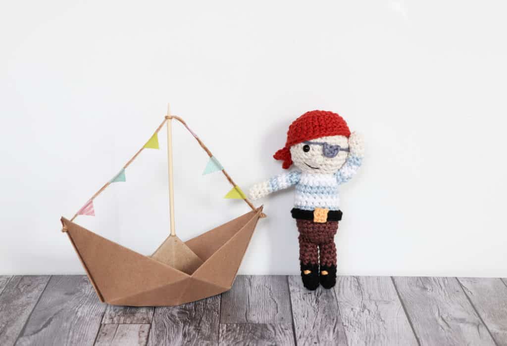 crochet pirate pattern | happy hand made crochet pirate standing next to a boat, pirate amigurumi, crochet gift for boys