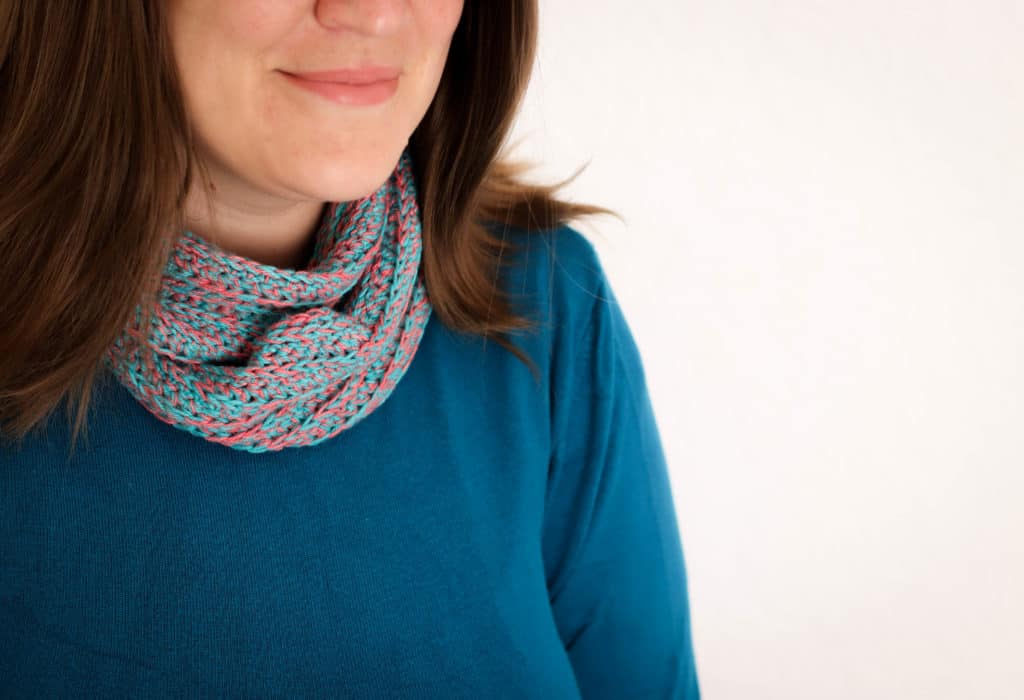 Close up of an crochet infinity scarf, in teal and watermelon