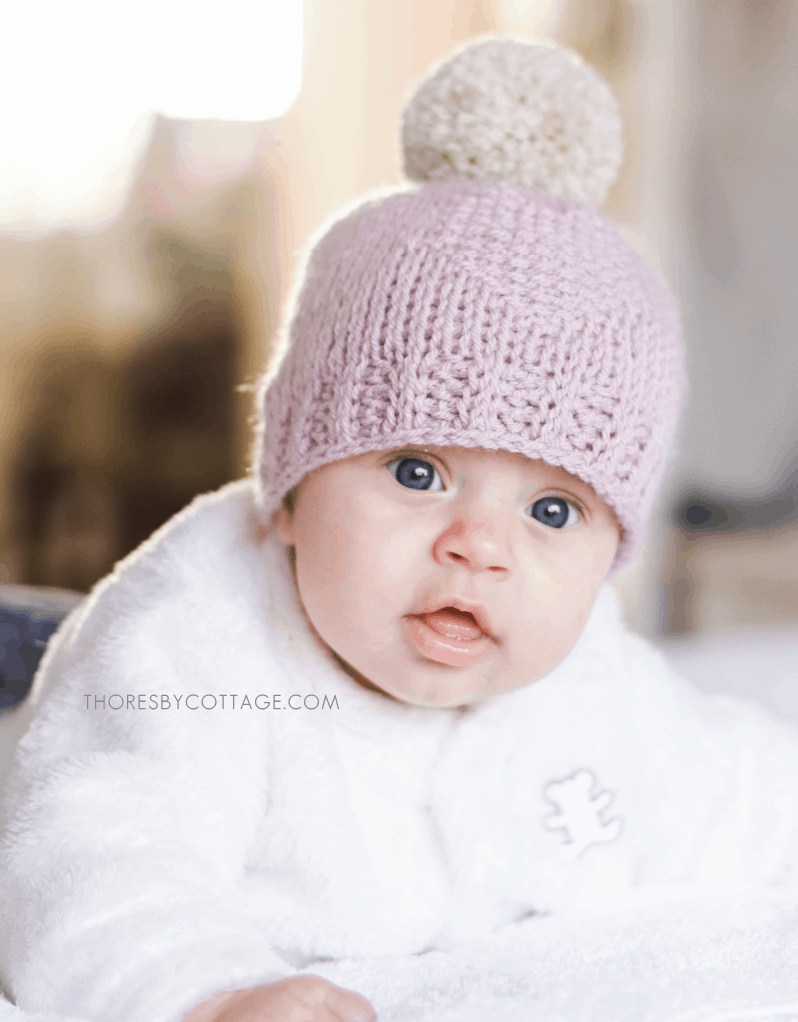 Blue eyes baby with a pink crocheted hat topped with a large pom pom