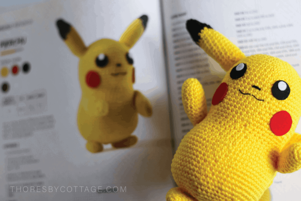 Crocheted Pikachu lying on a Pokémon crochet book