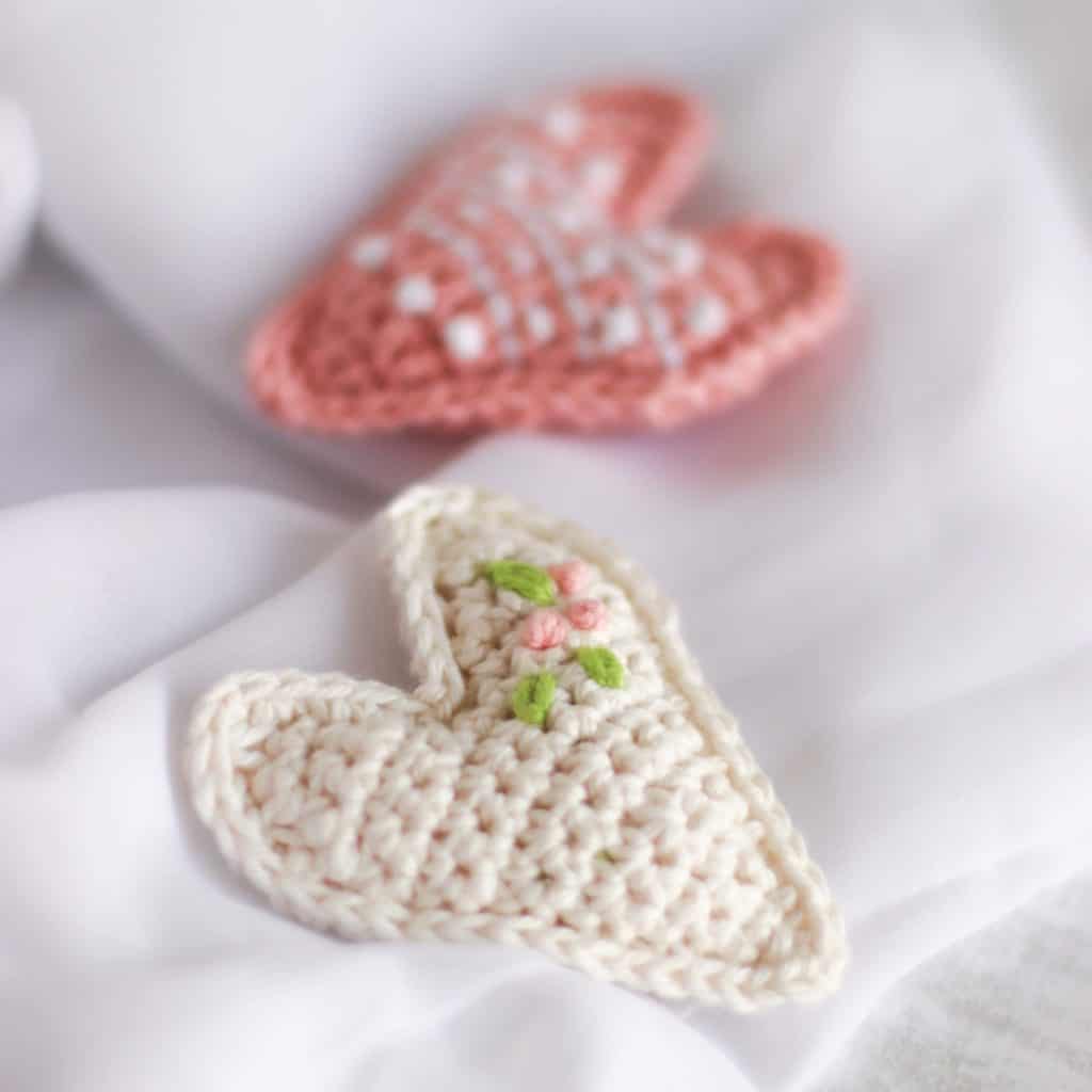 cream and pink crocheted hearts with flowers embroidered on them. Embroidered crochet heart