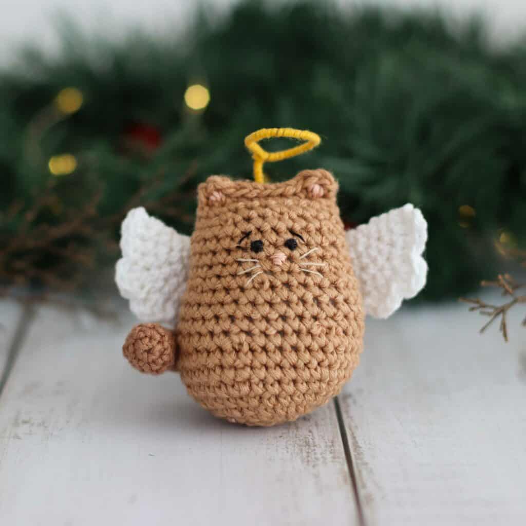 Itty Bitty Angel Kitty | Crochet Angel Cat Pattern crochet angel cat pattern with white wings and a halo, surrounded by green foliage.