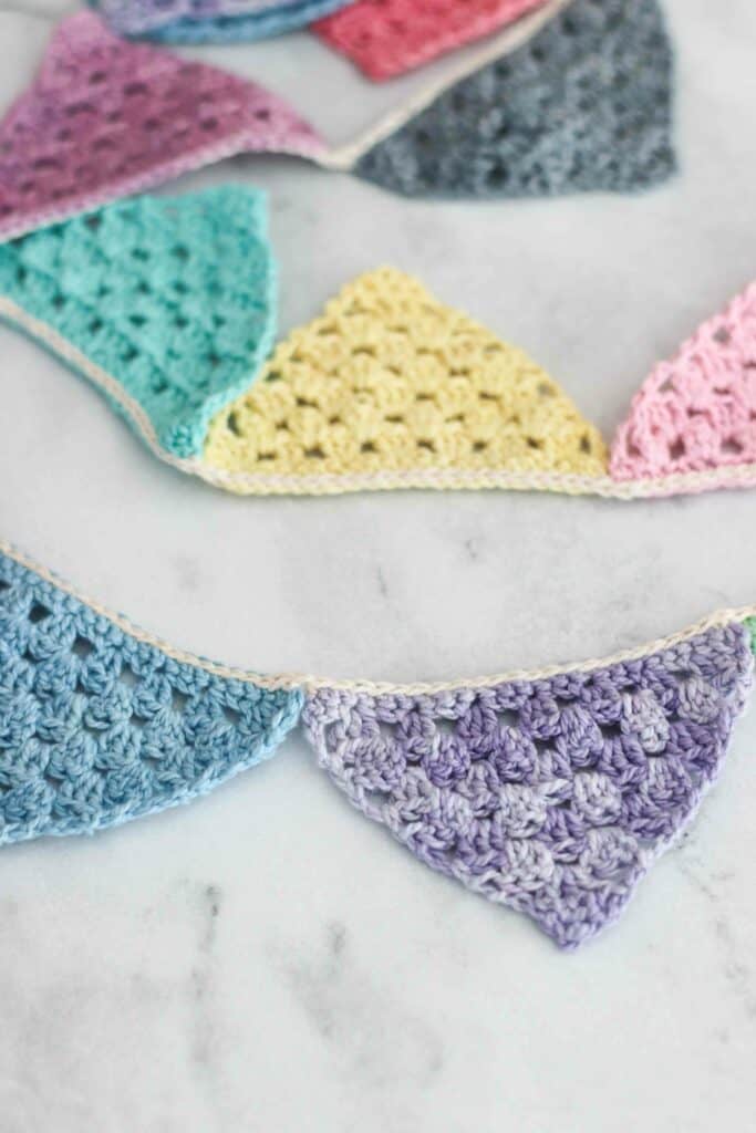 Granny stitch crochet bunting pattern close up the finished item made from the crochet bunting pattern | macaron colored crochet triangles joined together as bunting